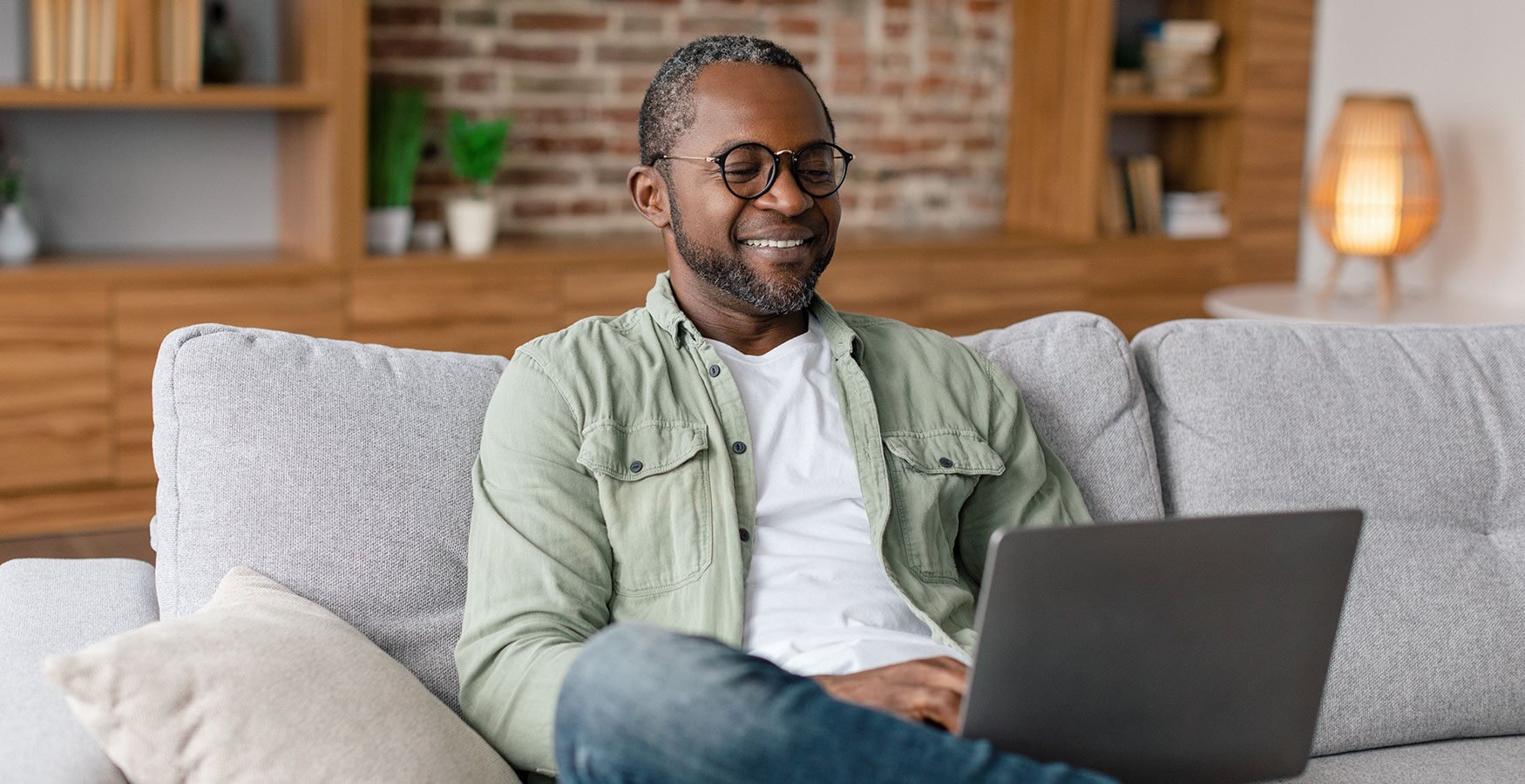 Man smiling while using a laptop on a couch in a cozy living room.