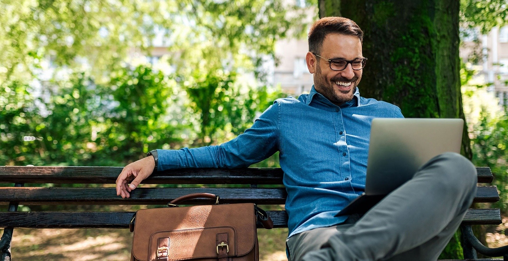 Smiling man sitting on a park bench on his computer.