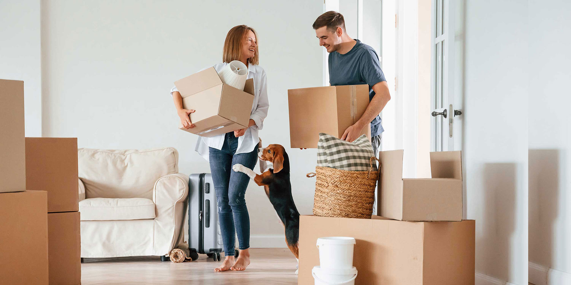 Couple holding moving boxes. Their dog standing against woman's leg.